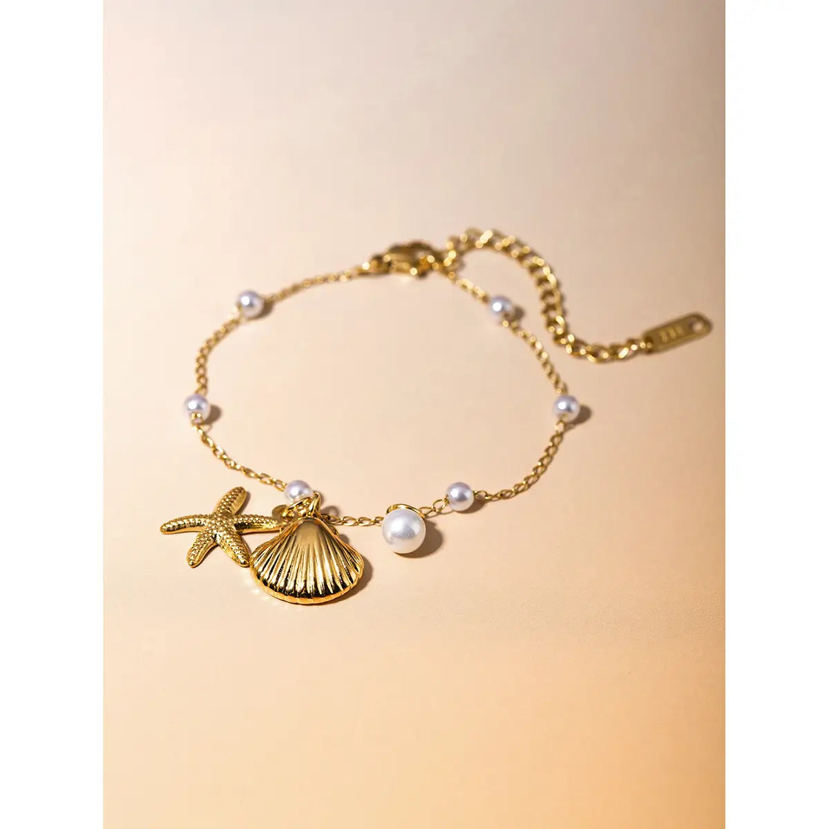 18k gold plated bracelet featuring starfish and seashell charms accented with small white pearls on an elegant gold-toned chain.
