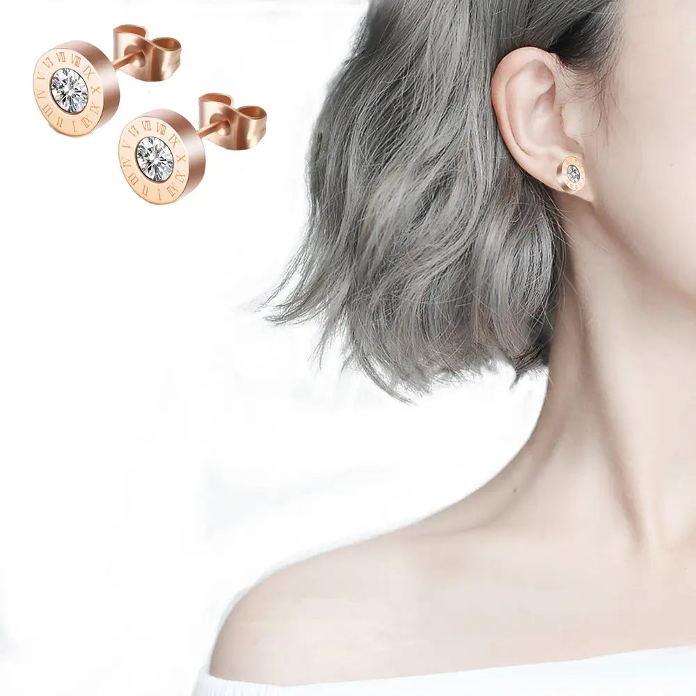 Boucles d’oreilles à tige en diamant en or rose, motif de chiffres romains, comprenant un diamant central transparent et des chiffres romains détaillés disposés tout autour du bord.