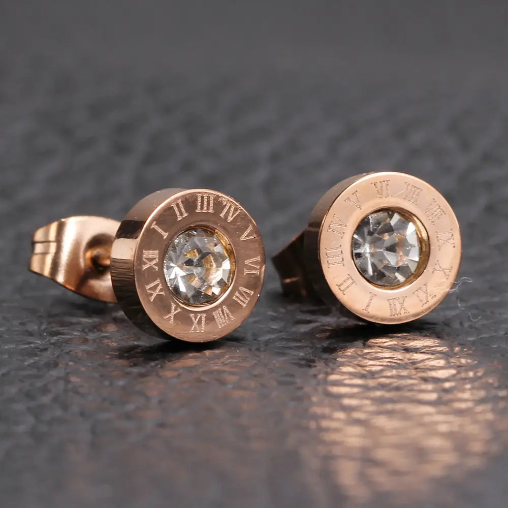 Boucles d’oreilles à tige en diamant en or rose, motif de chiffres romains, comprenant un cristal transparent central entouré d’une monture ajourée de chiffres romains gravés.