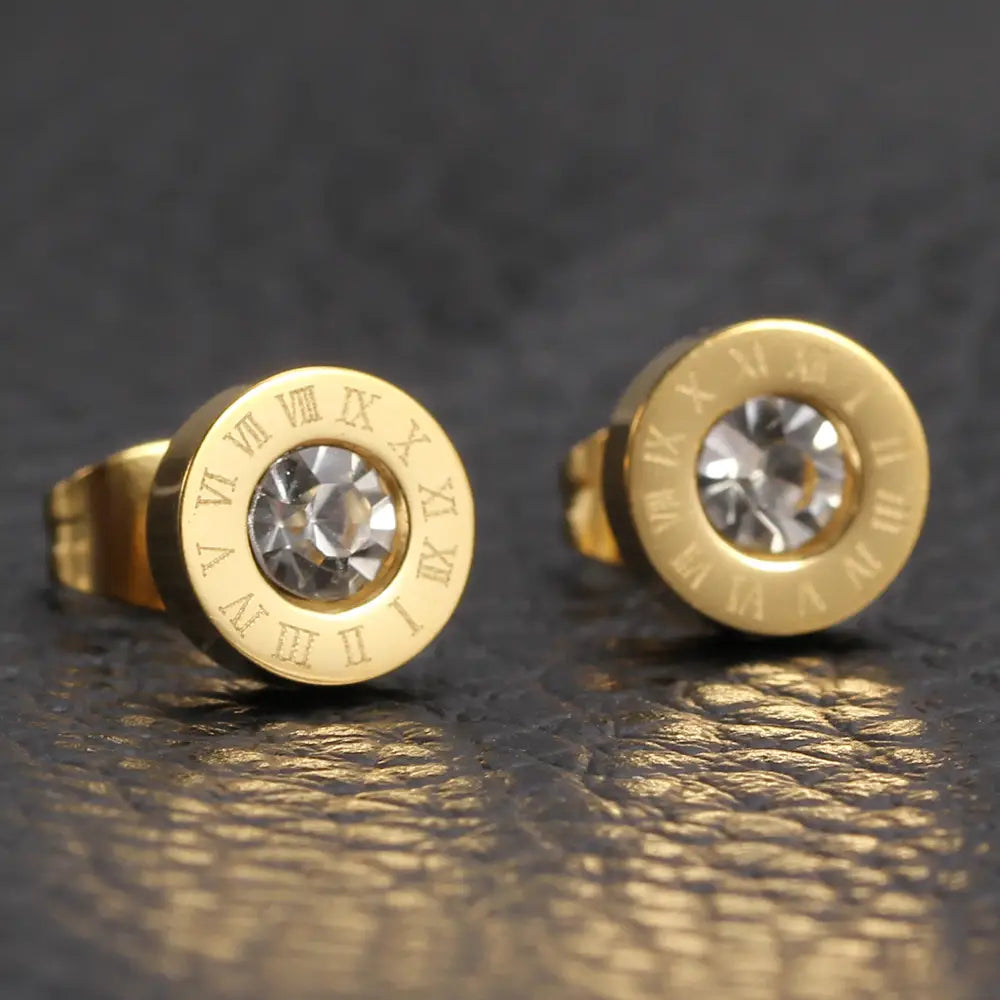 Boucles d’oreilles à tige en or rose, motif de chiffres romains, avec des centres en cristal transparent dans une parure de boucles d’oreilles à tige en diamant.