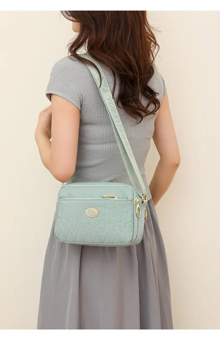 Light green crocodile-textured quilted crossbody bag with gold hardware and matching strap.