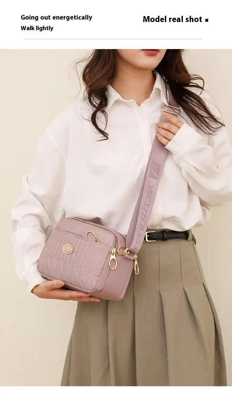 A soft lavender quilted crossbody bag with a textured surface and gold-tone hardware and strap.