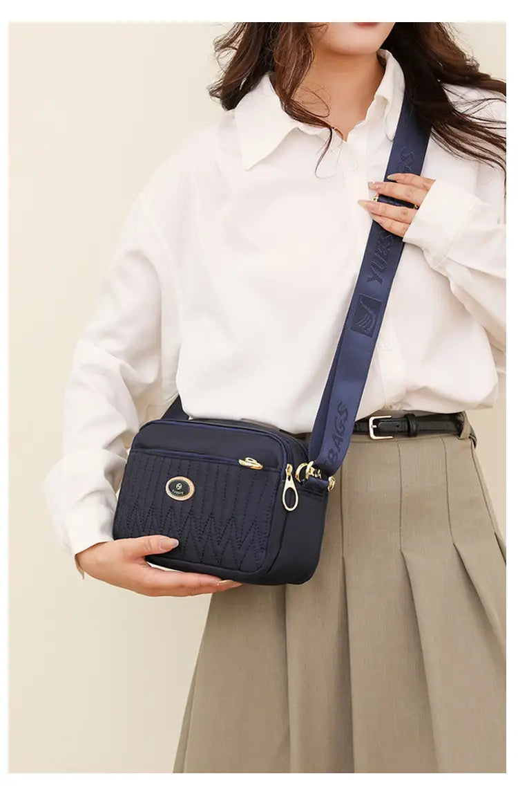 Navy blue quilted crossbody bag with gold-tone hardware and a branded strap designed for stylish everyday use.
