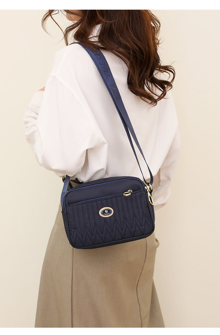 Navy blue quilted crossbody bag with gold-tone hardware and a circular logo plaque designed for stylish everyday use.