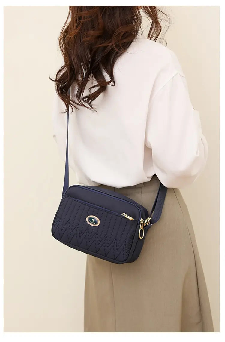 Navy blue quilted crossbody bag with gold hardware and circular logo emblem designed for hands-free carrying.