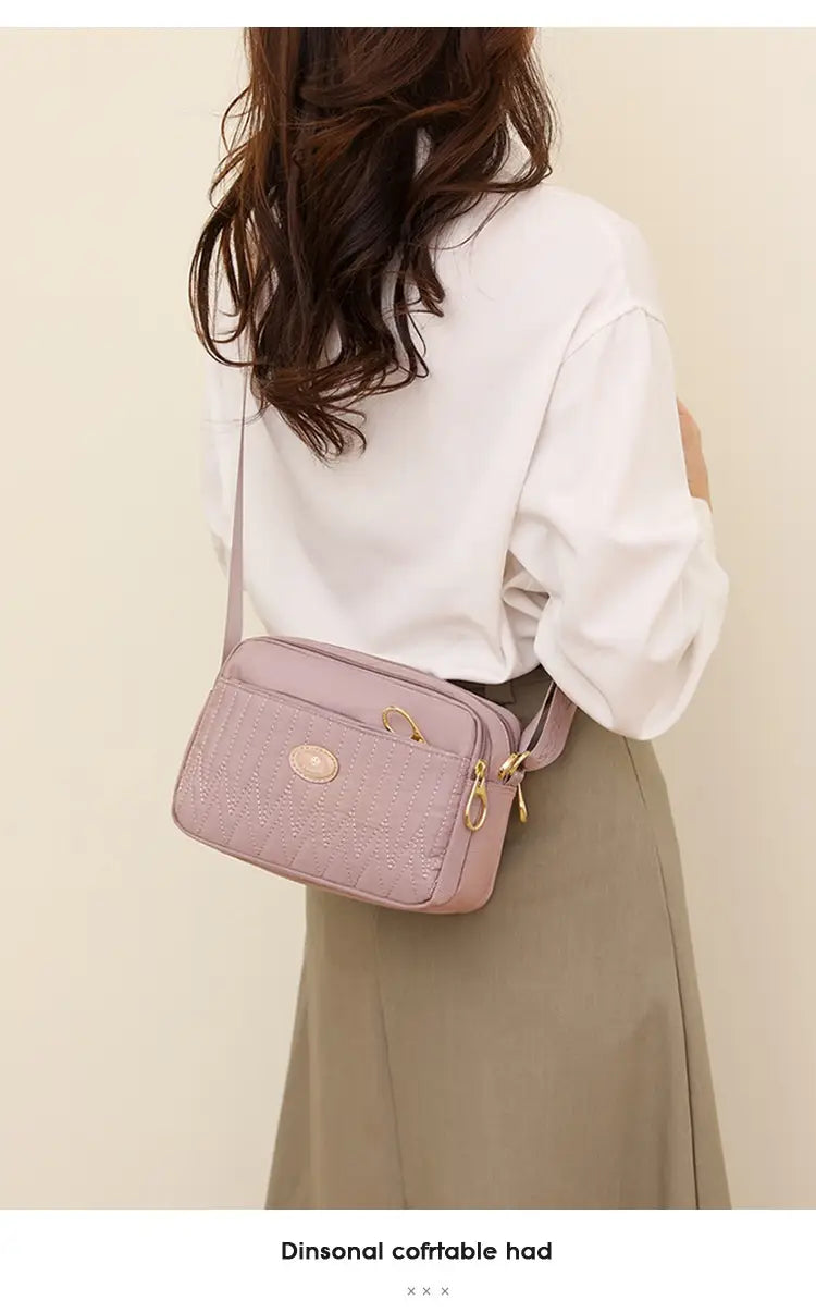 A soft lavender quilted crossbody bag with gold hardware and strap made of textured material.