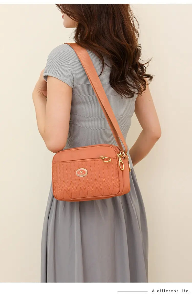 Orange textured quilted crossbody bag with gold hardware and a circular logo emblem designed for stylish everyday use.