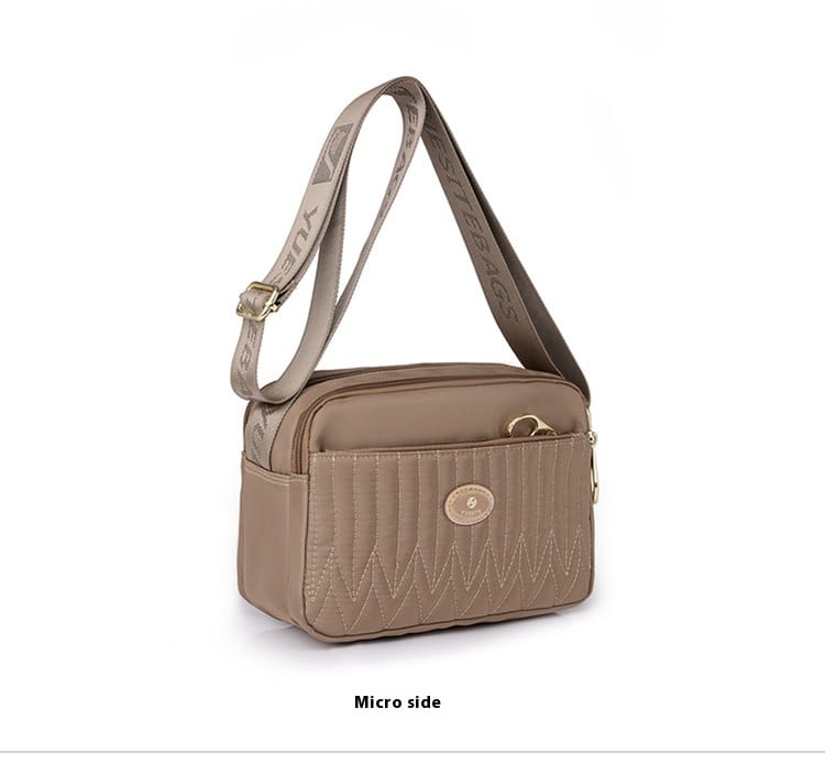 Beige quilted crossbody bag with zigzag stitched front panel and branded strap featuring gold hardware.