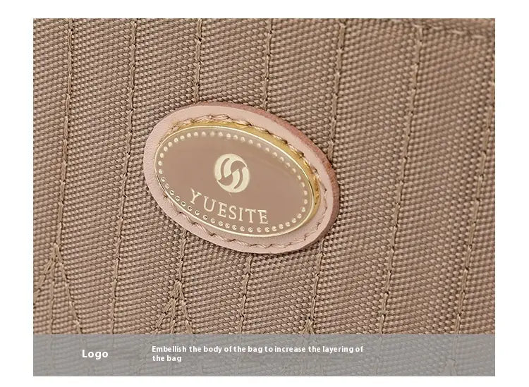 Beige textured fabric quilted crossbody bag with gold hardware and strap featuring a pink oval leather patch with the yuesite logo in gold lettering.