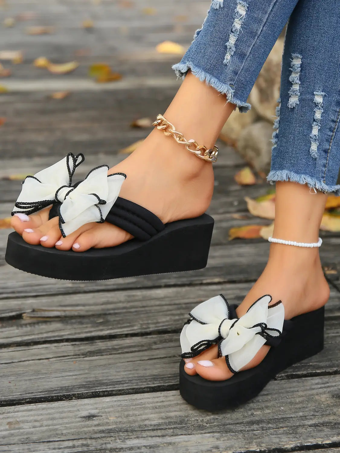 Sandalias tipo plataforma negras con gran adorno de moño transparente blanco con ribete negro en la parte superior.