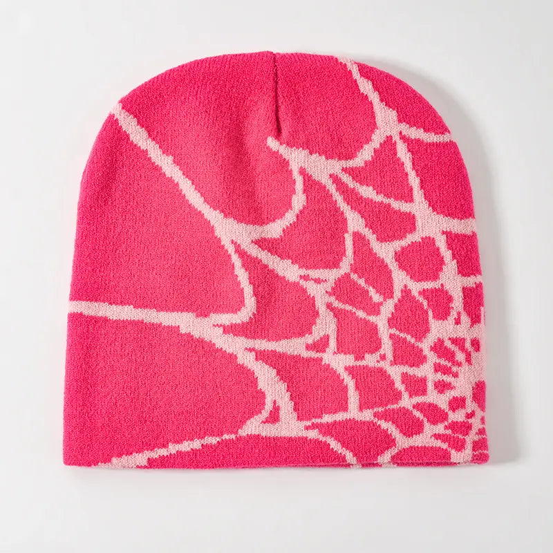 A vibrant pink knit beanie featuring a bold white spiderweb pattern designed as a winter hat.