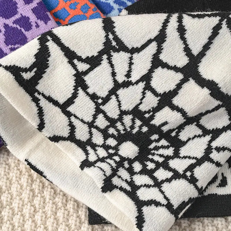 A cream-colored knit sock with a bold black spiderweb pattern matching the spiderweb knit beanie winter hat.