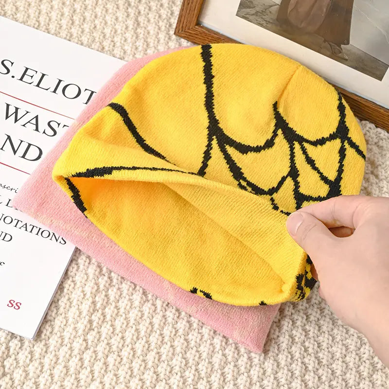 Yellow knit beanie with black spiderweb pattern designed as a winter hat for cold weather use.