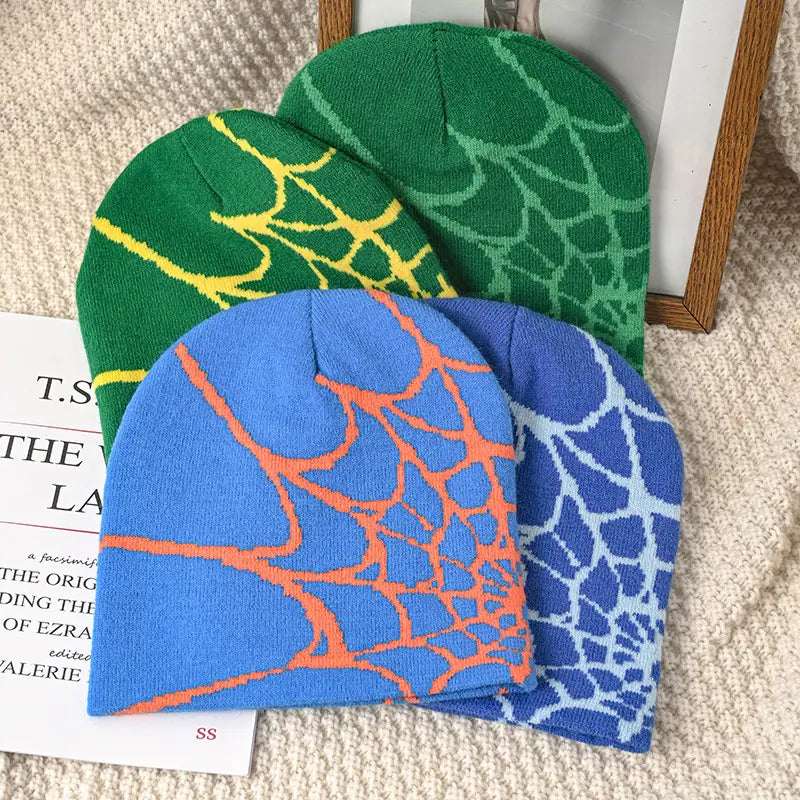 Three knitted spiderweb knit beanie winter hats in green, blue, and lighter blue designed for cold weather.