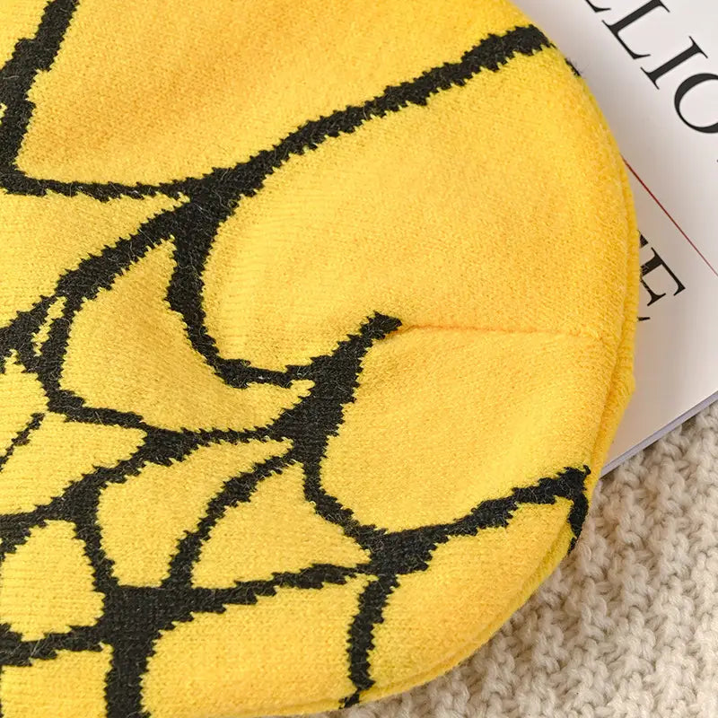 Yellow knit beanie with black spiderweb pattern designed as a winter hat for cold weather.