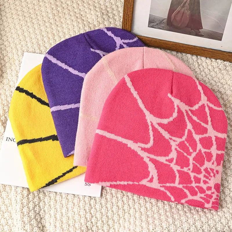 A vibrant pink knit spiderweb beanie featuring a white spiderweb pattern designed as a winter hat.