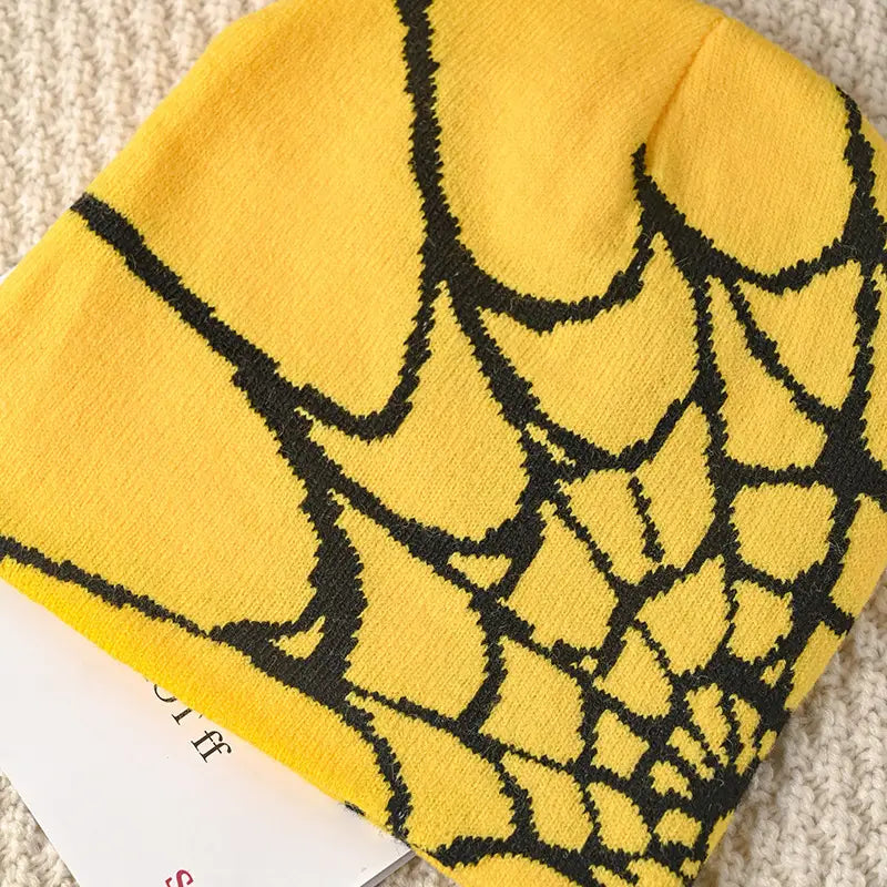 Bright yellow knit spiderweb beanie featuring a bold black pattern designed for winter wear.
