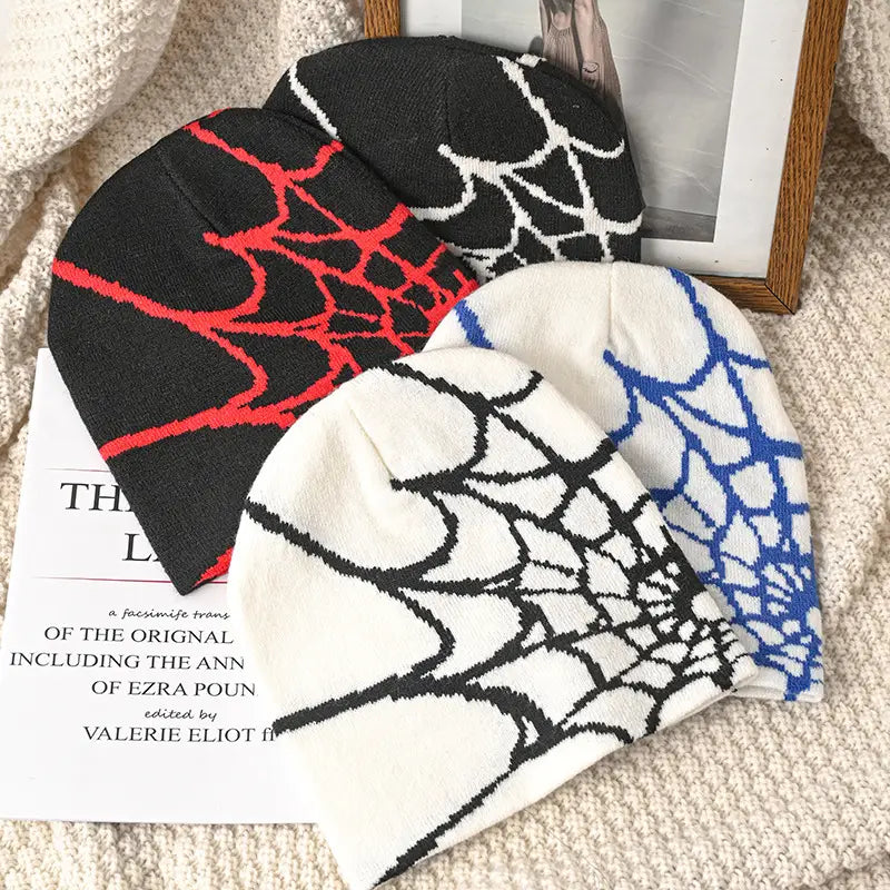 Three knitted spiderweb knit beanie winter hats in black red and blue featuring spiderweb patterns on white and dark bases.