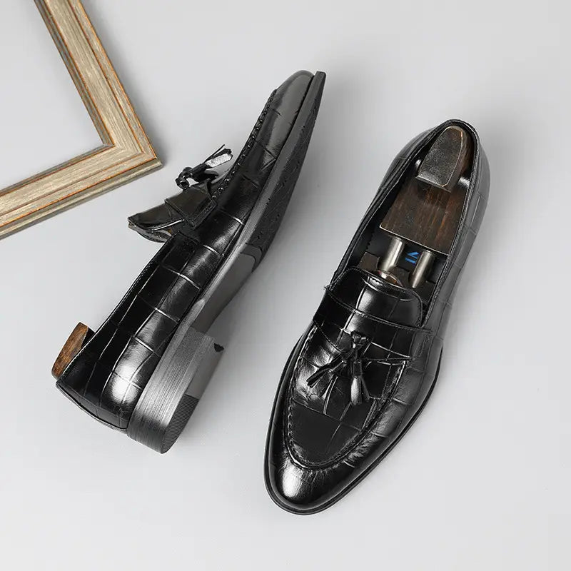Mocasines de cuero con estampado de cocodrilo negro con borlas, mostrados desde la parte trasera, con un acabado texturizado de lujo.