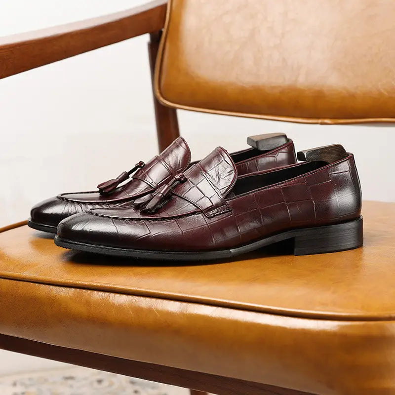 Mocasines con borlas de cuero con estampado de cocodrilo color burdeos con tacón bajo, mostrados desde la parte trasera.