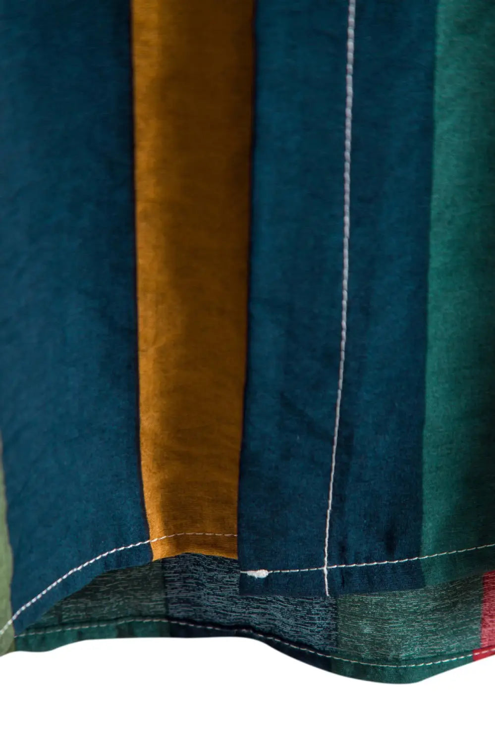 A close-up of a striped short sleeve button up shirt featuring vertical stripes in deep teal mustard yellow and forest green with contrasting white stitching along the hem.