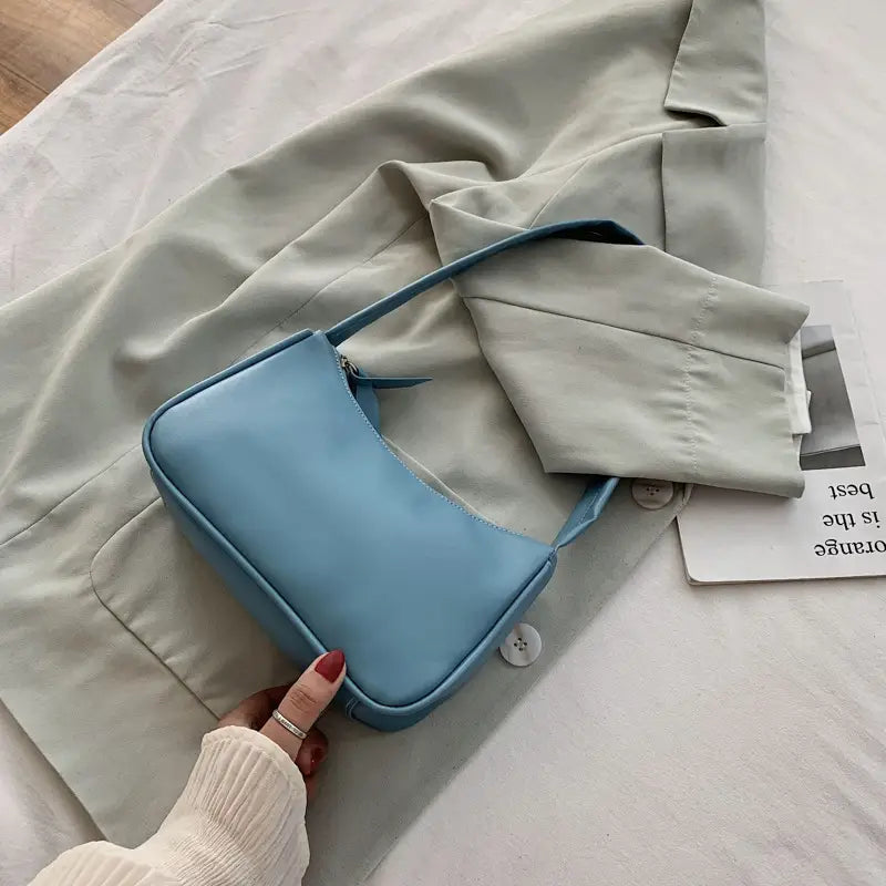 A sleek light blue underarm shoulder bag made of faux leather with a smooth, structured rectangular design and a matching shoulder strap.