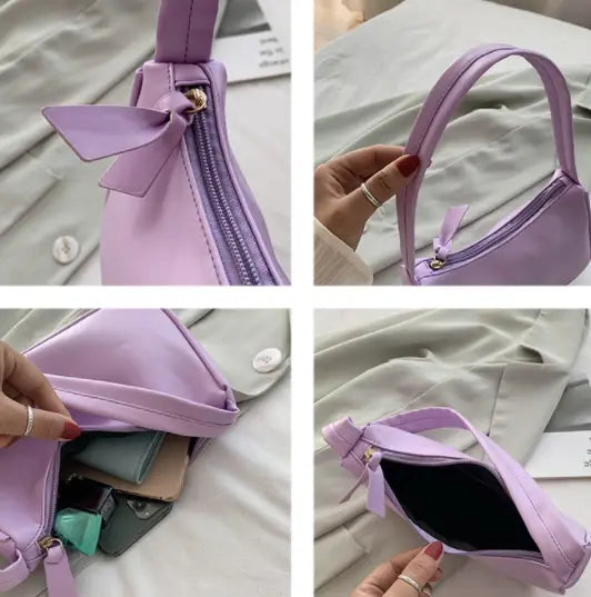 A lavender-colored underarm shoulder bag mini handbag made of soft synthetic leather with a decorative bow at the zipper pull.
