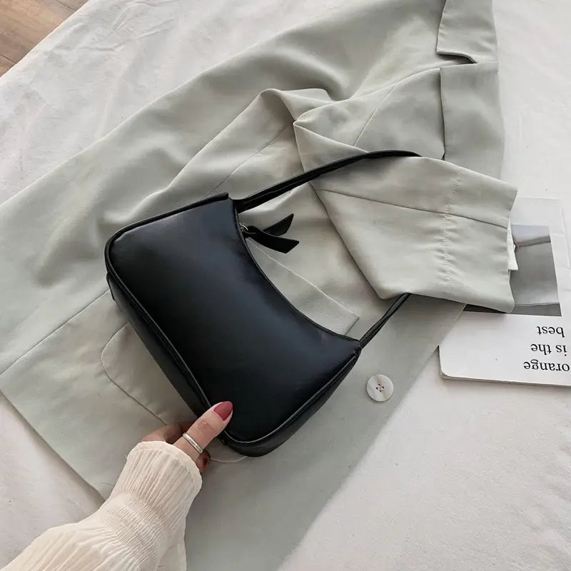Black faux leather underarm shoulder bag with a sleek minimalist design and a small black bow accent rectangular purse.