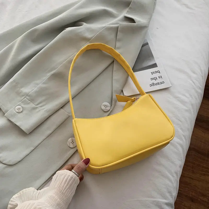 A vibrant yellow smooth textured underarm shoulder bag made of faux leather with a single curved handle and minimalist rectangular design.