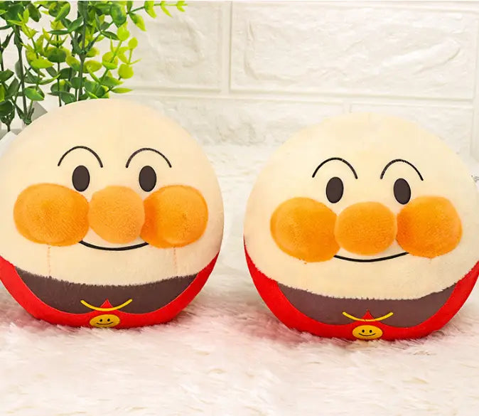 two round plush anpanman character pillows with cream-colored faces, orange cheeks and nose, red and brown bodies, and yellow smiley face emblems featured as part of a plush jumping ball interactive talking bunny toy product.