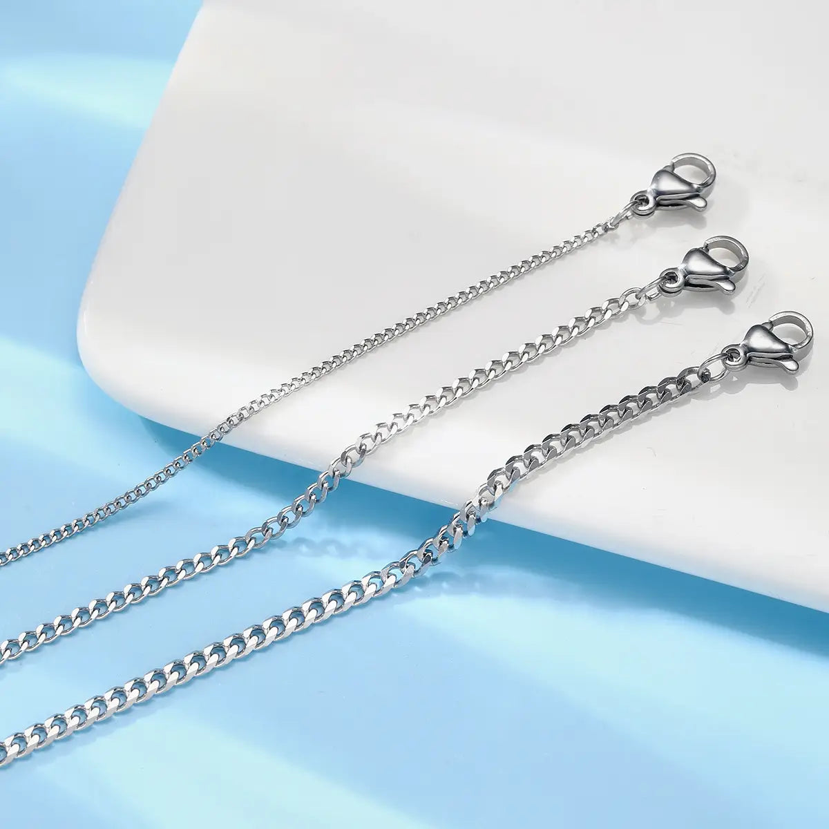Three silver-toned curb chain necklaces with lobster clasps displayed on a white surface from the unisex silver layered Cuban and Figaro link bracelet set.