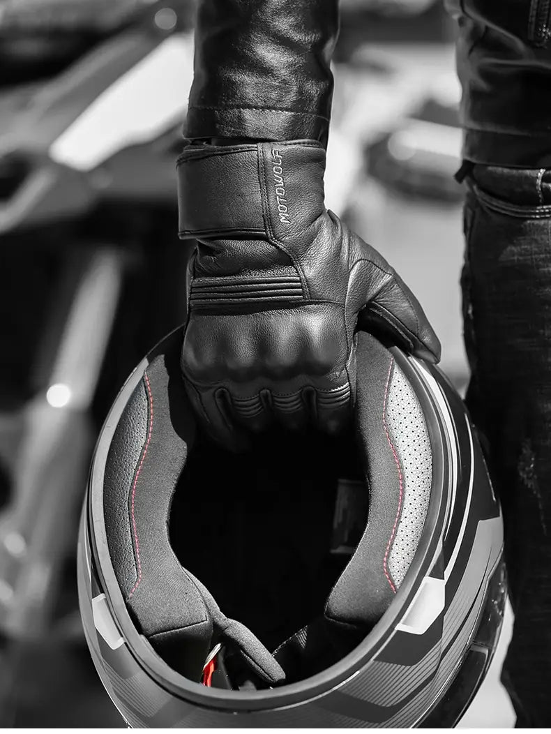 Black leather men winter motorcycle glove with motogurt branding on the wrist strap worn by a rider holding an open helmet.
