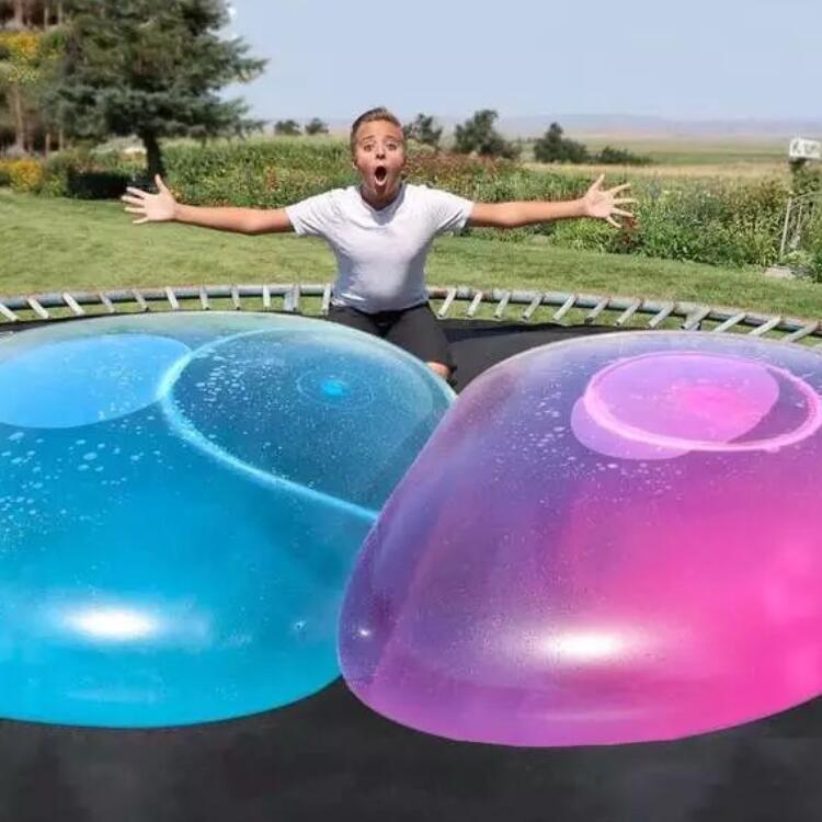 Dos bolas hinchables de burbuja gigantes translúcidas de TPR, tipo globos de agua elásticos, que son descansan sobre un trampolín en azul vibrante y rosa brillante.