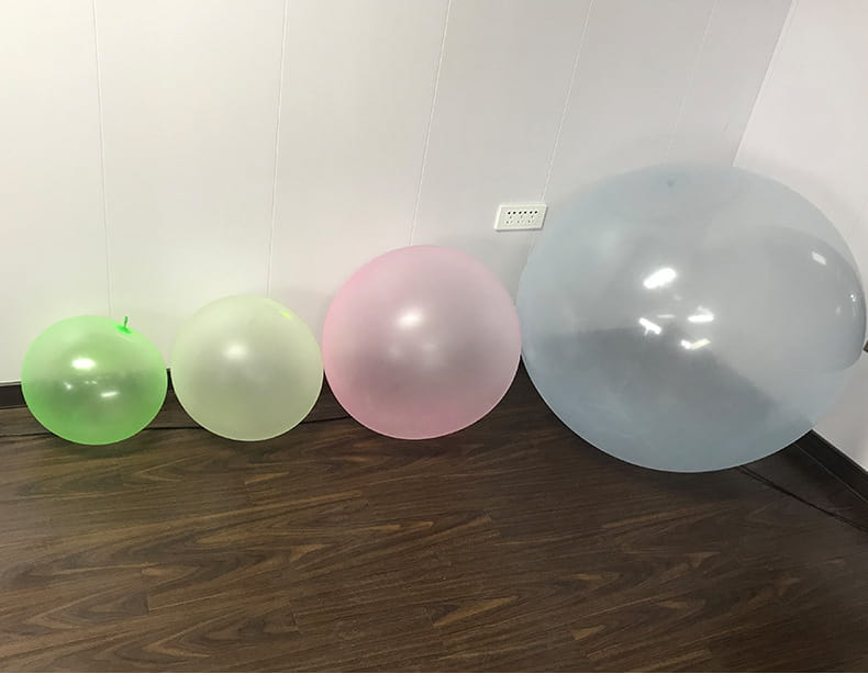 Cuatro bolas hinchables de burbuja gigantes translúcidas de TPR, tipo globos de agua elásticos, en tonos verde, amarillo pálido, rosa y azul claro, dispuestas una al lado de la otra sobre un suelo de madera.