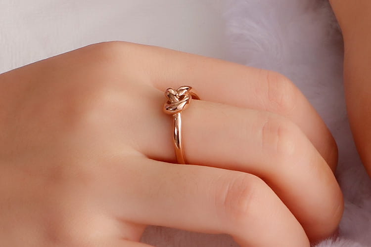 A delicate rose gold geometric truelove knot ring with a slender band and intricate twisted design made of titanium steel.