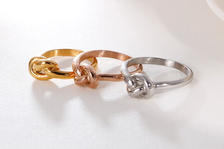 Three metallic geometric truelove knot titanium steel rings in gold rose gold and silver finishes.