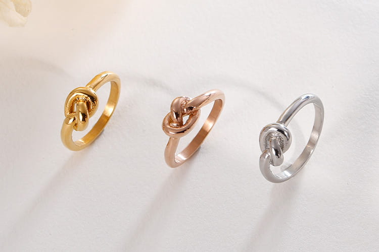 Three geometric truelove knot titanium steel rings in gold rose gold and silver finishes.
