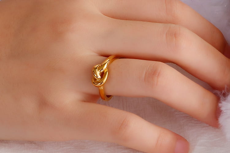 A delicate gold geometric truelove knot ring made of titanium steel worn on a finger.