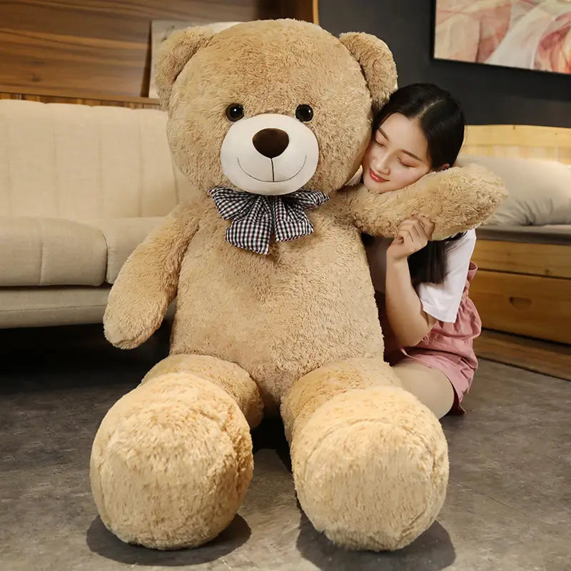 Ein flauschiger Teddybär aus hellem Braun als Plüschtier mit weißem Schnäuzchen, schwarzen Knopfaugen und einer karierter Fliege.