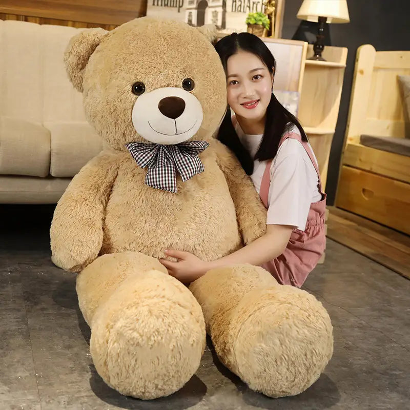 Ein flauschiger Teddybär aus hellem Braun als Plüschtier mit weißem Schnäuzchen, schwarzen Knopfaugen und einer mit einer karierter Fliege verzierten braunen Nase.