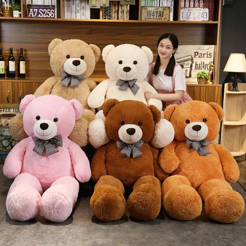 Ein Teddybär-Plüschtier mit weichem rosafarbenem Fell, schwarzen Knopfaugen, einer kleinen braunen Nase und einer karierter Fliege.