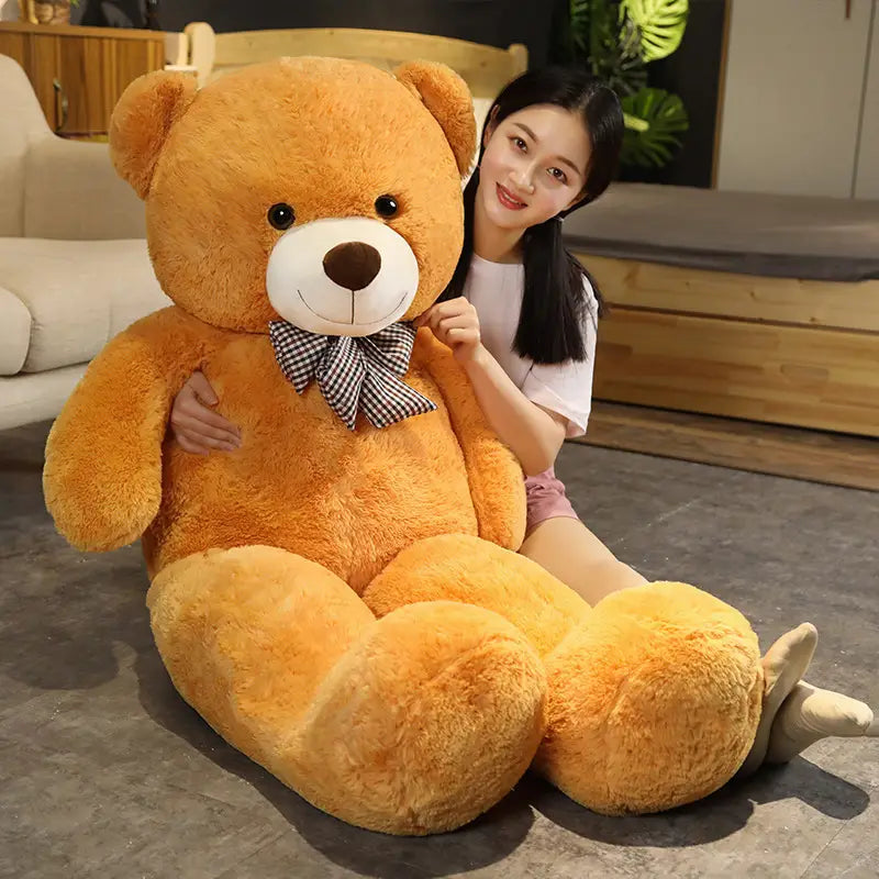 Ein flauschiger goldbrauner Teddybär als Plüschtier mit weißem Schnäuzchen und schwarzen Knopfaugen, der eine karierte Fliege trägt.