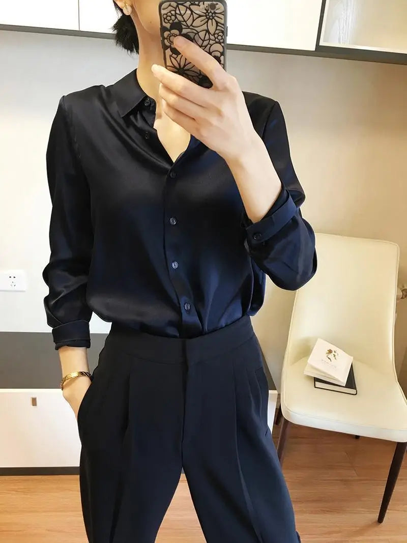 A sleek navy blue satin long sleeve button down silk blouse with a classic collar and rolled cuffs.