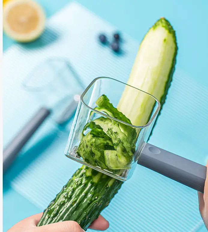 Éplucheur de légumes en acier inoxydable avec une poignée gris mat, épluchant la peau verte d’une courgette (concombre) vert foncé.