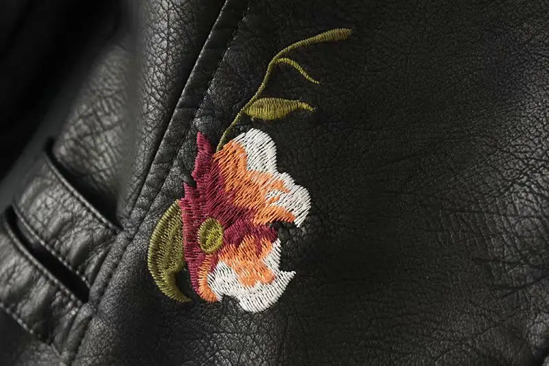 A floral embroidered studded leather moto jacket featuring a vibrant flower patch with maroon orange and white petals stitched onto black leather.