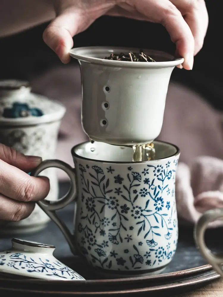 A white ceramic tea strainer with blue floral patterns and a handle featuring small holes for steeping leaves is part of the ceramic tea mug with infuser and lid floral 300ml.