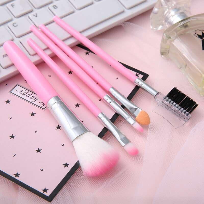 Ensemble de cinq pinceaux de maquillage à manche rose, avec viroles en argent et poils dégradés roses, comprenant un grand pinceau duveteux et un pinceau à sourcils coudé pour une application précise.