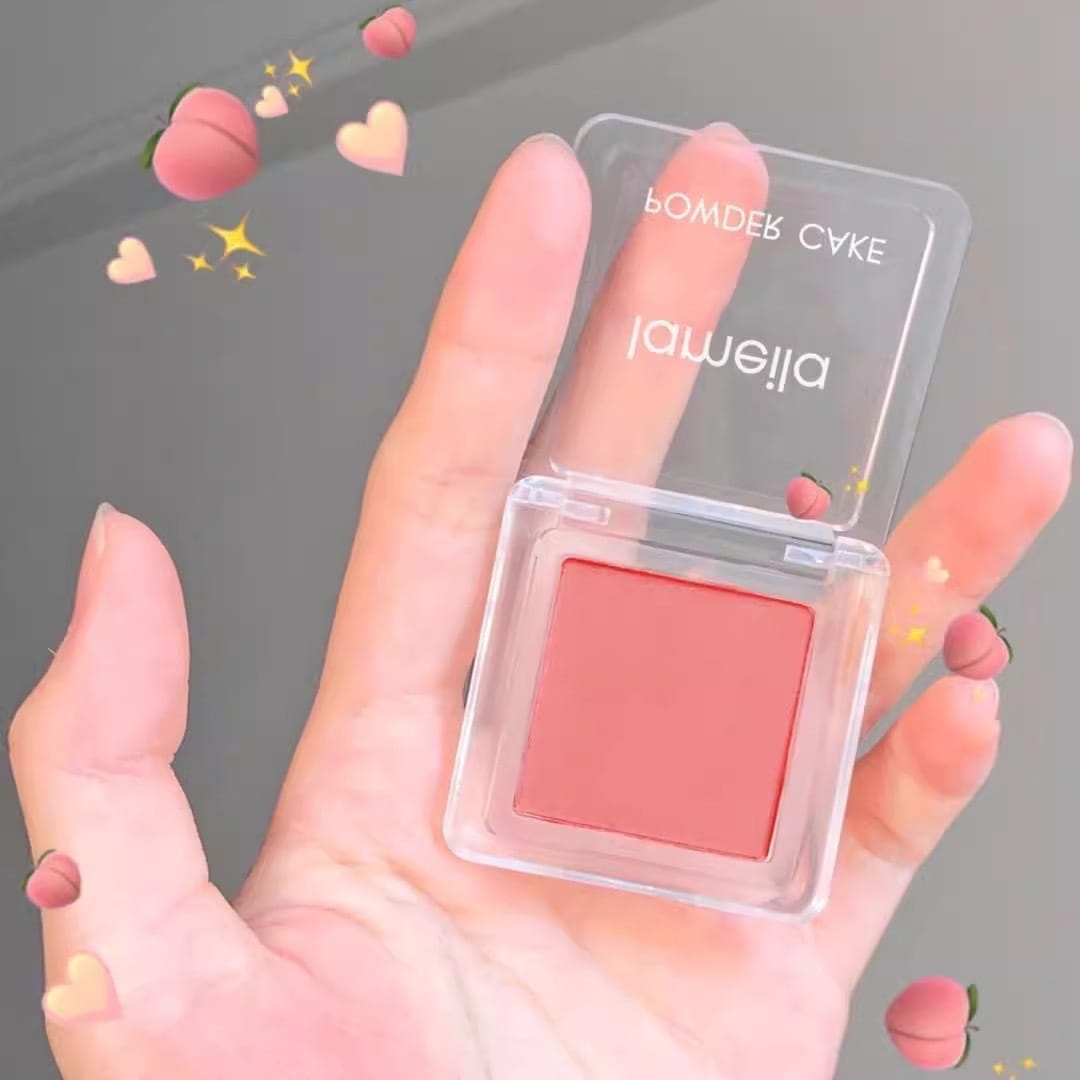 a translucent square compact blush labeled powder cake and jameilla containing soft pink powder as part of the monochrome powder blush compact with brush in four colors