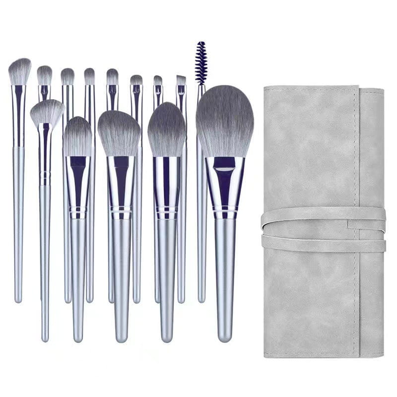 makeup brush set with 15 silver-handled pieces with gray and white bristles neatly arranged beside a matching light gray suede carrying case