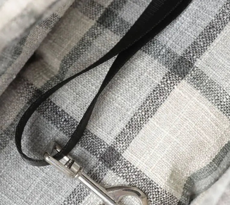 Black leather leash with silver metal clasp attached to a plaid pet carrier bag breathable travel dog purse.